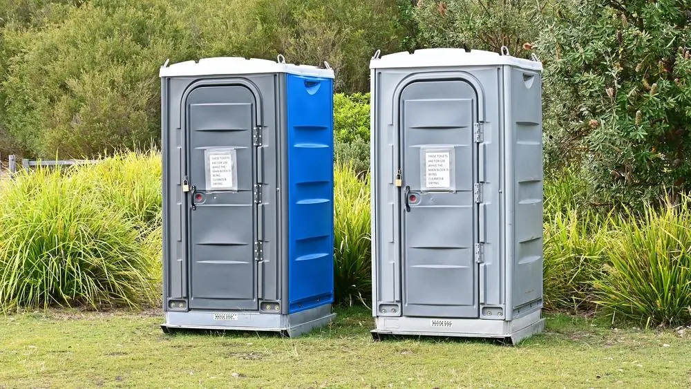 Two portable toilets placed on grass beside shrubs