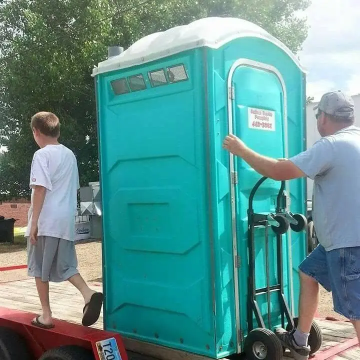 A portable toilet being moved from a trailer for delivery